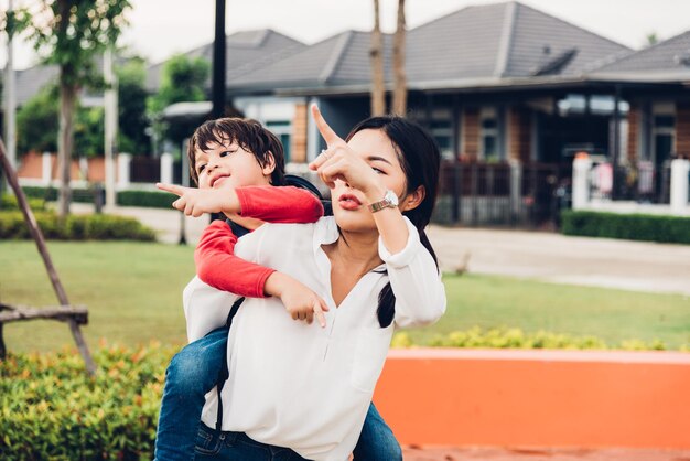 family happy children kid son boy kindergarten playing ride back piggyback mother mom on outdoors park