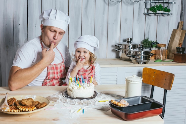 Семья, счастливая дочь с папой дома на кухне смеются и зажигают свечи на именинном торте