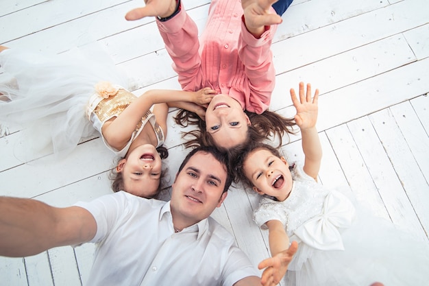 Family happy mom, dad and two girls twin sisters at home on a white wooden floor doing a selfie.