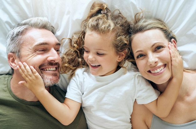 Famiglia felice e sorriso di persone dall'alto a letto a casa rilassarsi in una camera da letto madre ragazza e uomo con felicità insieme in una casa con amore cura e calma sorridente con una mentalità positiva