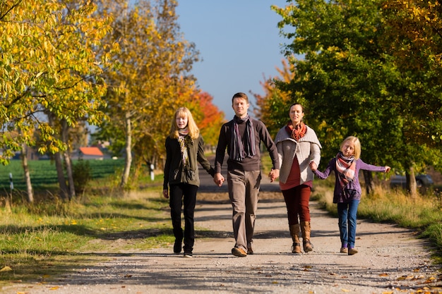 가을에 화려한 나무 앞에서 산책하는 가족