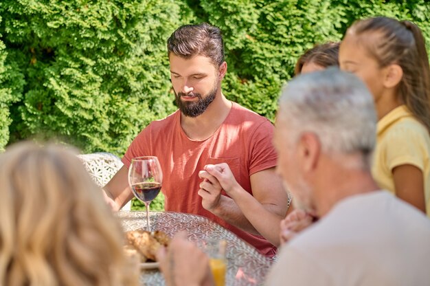 Una famiglia che si tiene per mano e prega insieme prima di cena