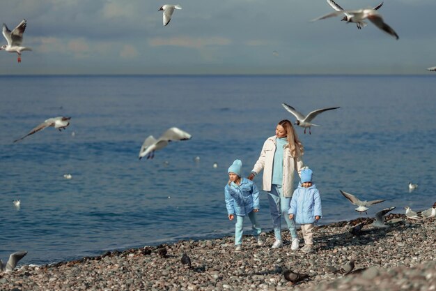 カモメに餌をやる海のそばを散歩する暖かい服を着た2人の娘を持つ家族の休日の母親