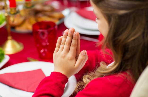 family, holiday, religion, tradition and people concept - close up of girl praying at christmas dinner at home