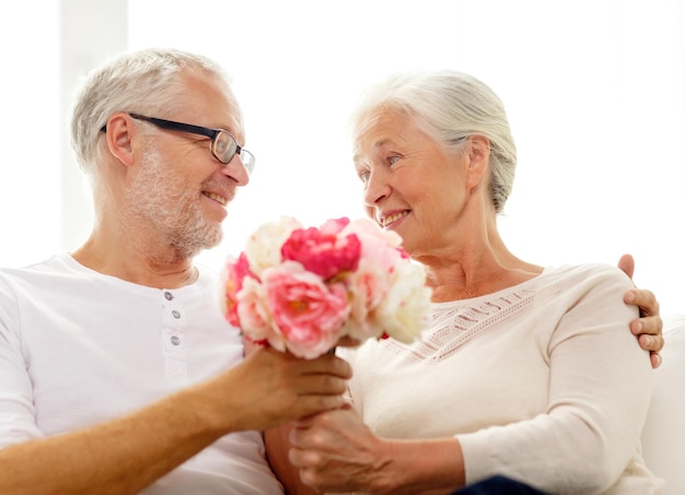 家族、休日、年齢、人々の概念-家にたくさんの花を持つ幸せな年配のカップル