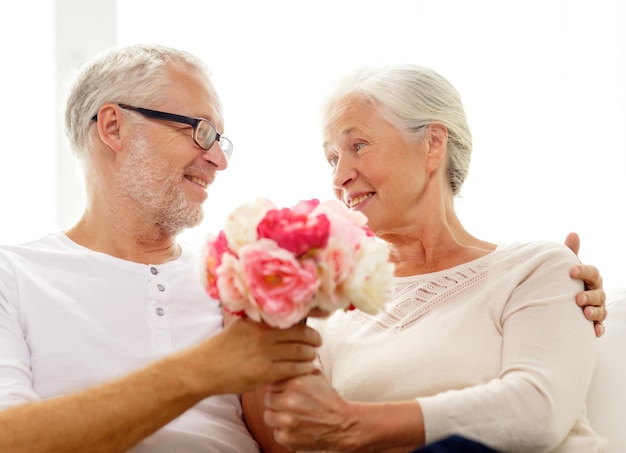 family, holidays, age and people concept - happy senior couple with bunch of flowers at home