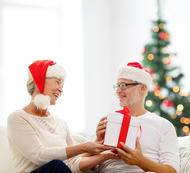 family, holidays, age and people concept - happy senior couple with gift box over living room and christmas tree background