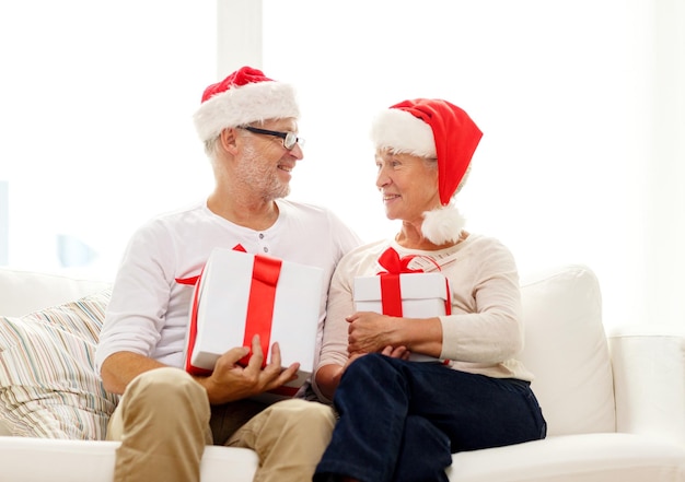 family, holidays, christmas, age and people concept - happy senior couple in santa helper hats with gift boxes at home