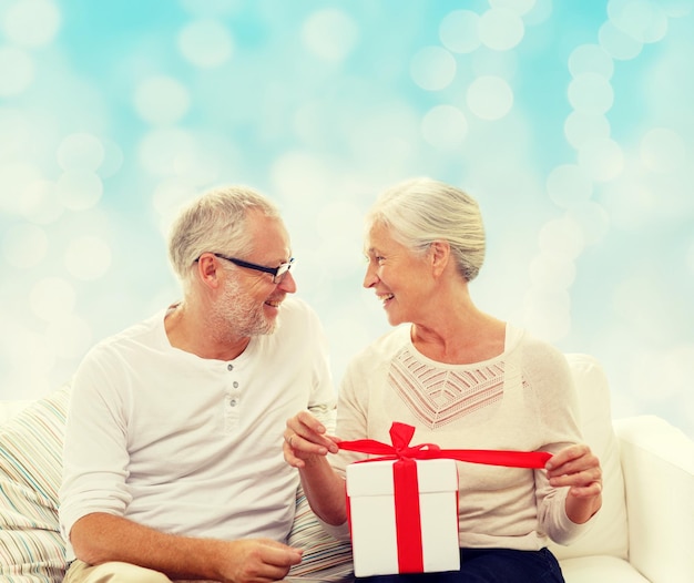 family, holidays, christmas, age and people concept - happy senior couple with gift box over blue lights background