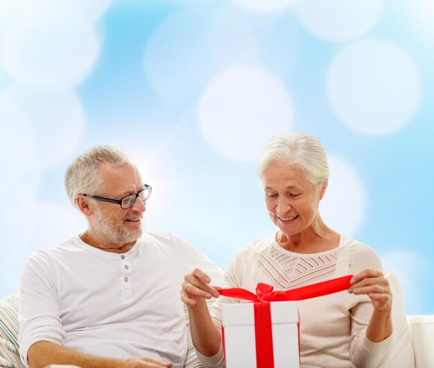 family, holidays, christmas, age and people concept - happy senior couple with gift box over blue lights background