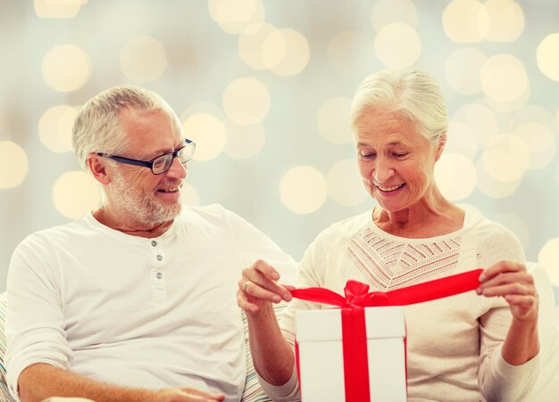 family, holidays, christmas, age and people concept - happy senior couple with gift box over holidays lights background