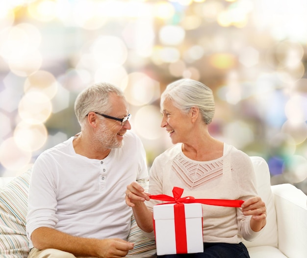 family, holidays, christmas, age and people concept - happy senior couple with gift box over lights background