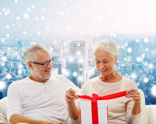 家族、休日、クリスマス、年齢、人々の概念-雪に覆われた街の背景にギフトボックスと幸せな年配のカップル