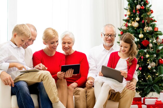 family, holidays, christmas, technology and people concept - smiling family with tablet pc computers sitting on couch at home