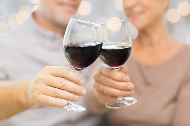 family, holidays, drinks, age and people concept - close up of happy senior couple clinking glasses with red wine over lights background