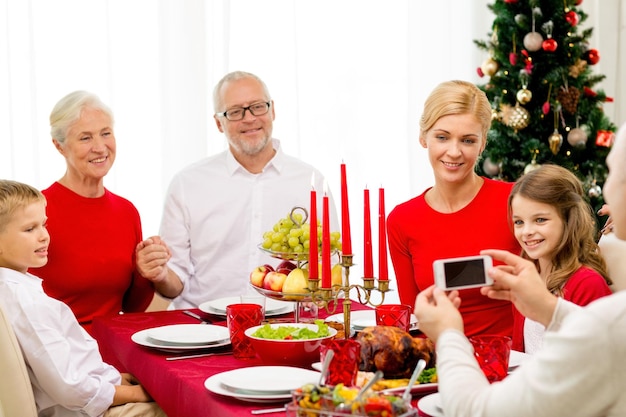 семья, праздники, поколение, рождество и концепция людей - улыбающаяся семья обедает и фотографируется с камерой дома