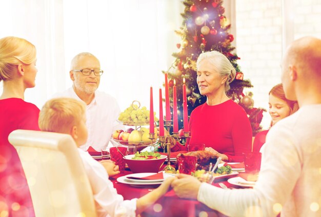 家族、休日、世代、クリスマス、人々の概念-夕食を食べて家で祈る笑顔の家族