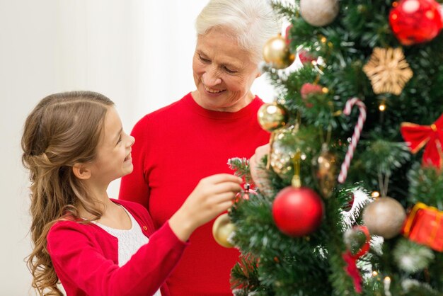 Concetto di famiglia, vacanze, generazione e persone - ragazza sorridente con la nonna che decora l'albero di natale a casa