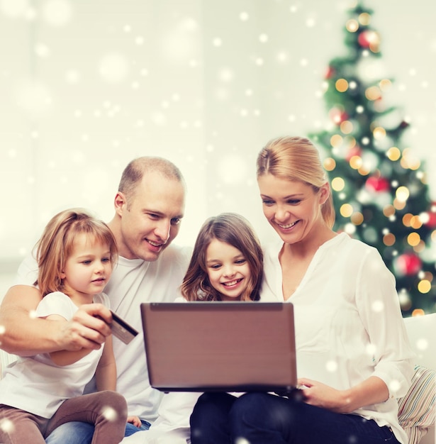 Famiglia, vacanze, shopping, tecnologia e persone - famiglia felice con computer portatile e carta di credito sul soggiorno, albero di natale e neve