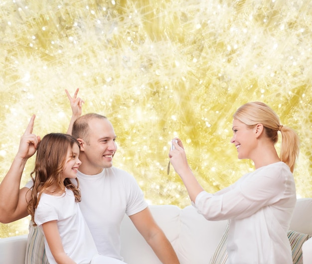 family, holidays, technology and people concept - smiling mother, father and little girl with camera over yellow lights background