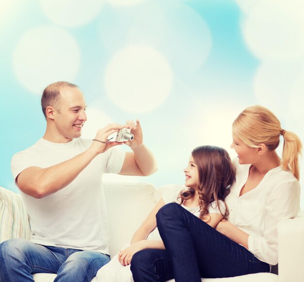 Foto famiglia, vacanze, tecnologia e persone - madre, padre e bambina sorridenti con la fotocamera su sfondo di luci blu