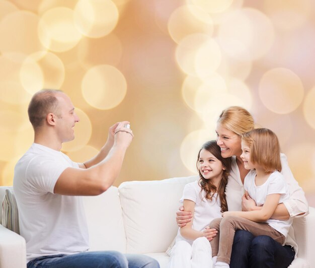 family, holidays, technology and people - smiling mother, father and little girls with camera over beige lights background