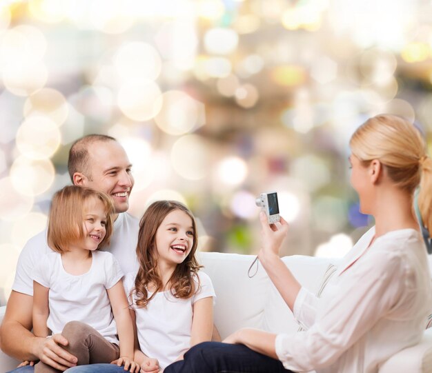 Famiglia, vacanze, tecnologia e persone - madre, padre e bambine sorridenti con la fotocamera su sfondo di luci