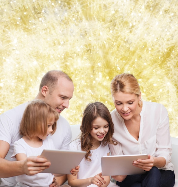 Photo family, holidays, technology and people - smiling mother, father and little girls with tablet pc computers over yellow lights background