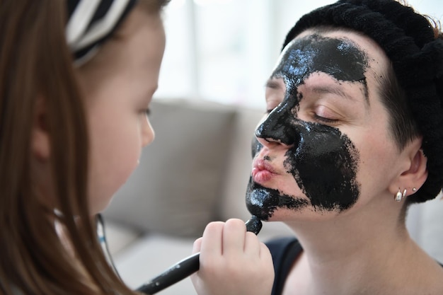 Family at home beauty treatment during coronavirus pandemic stay at home quarantine. Mother and little girl daughter  make a facial mask.