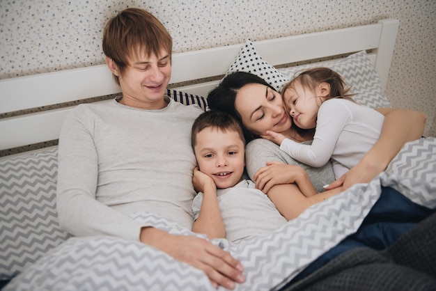 Family at home in pajamas. Daughter and son. Wake up in the morning. Hugging and kissing in the bedroom on the bed.