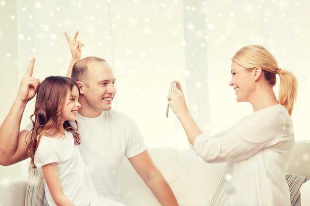 Famiglia, casa, tecnologia e persone - famiglia felice con la fotocamera che scatta foto su sfondo di fiocchi di neve