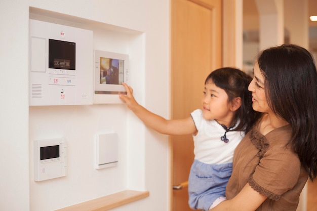 Photo family home a woman and her daughter looking at a screen on the wall controls of an entry phone or doorway