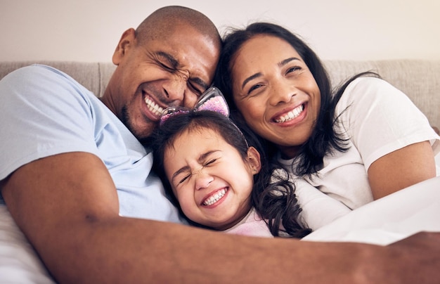 Family hug and happy on a bed at home with a smile comfort and security for quality time Man woman or latino parents and a girl kid together in the bedroom for morning bonding with love and care