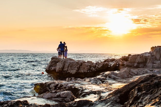 Family hugs on the rock beach, sunset on the sea