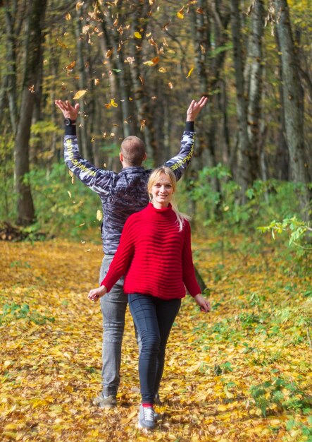 가을 숲의 낙엽 사이에 빨간 스웨터를 입은 가족 남편과 임신한 아내