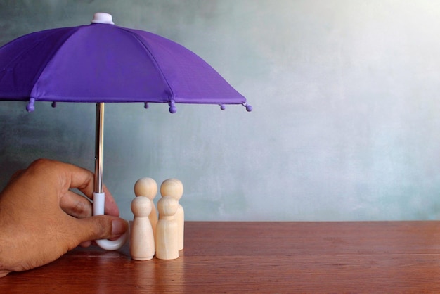 Family insurance concept Hand holding umbrella and wooden dolls with copy space