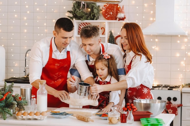 The family is standing in the Christmas kitchen and preparing dough for making cookies.