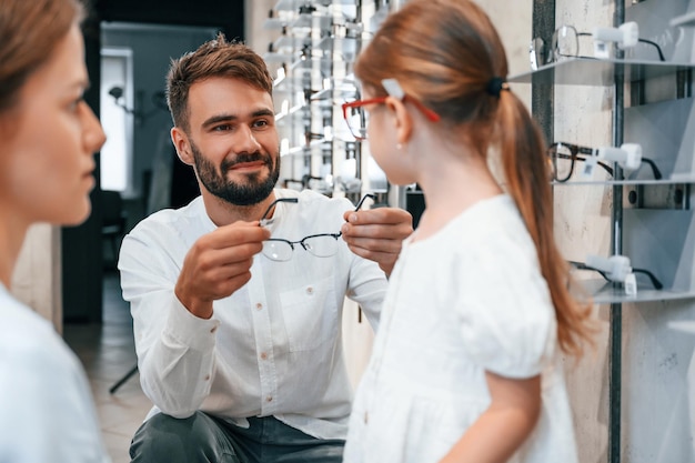 家族が一緒にいる 女性の男性と小さな女の子が視力を矯正するために正しい眼鏡を選んでいる