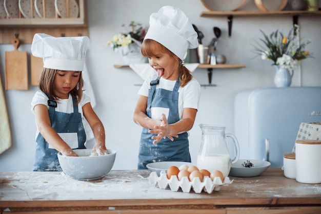 Family kids in white chef uniform preparing food on the kitchen.