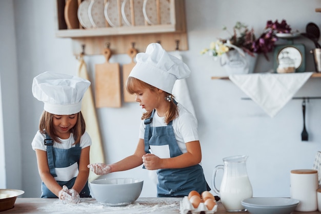 Family kids in white chef uniform preparing food on the kitchen.