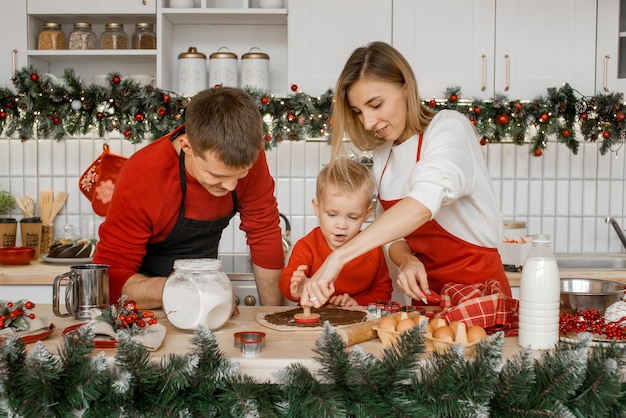 Family in the kitchen are very busy cutting raw dough with a cookie cutter on the table