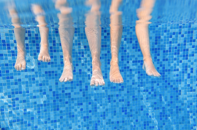 スイミングプールで水中の家族の足、水面白い概念、スポーツ、子供との休暇の下で子供と泳ぐ