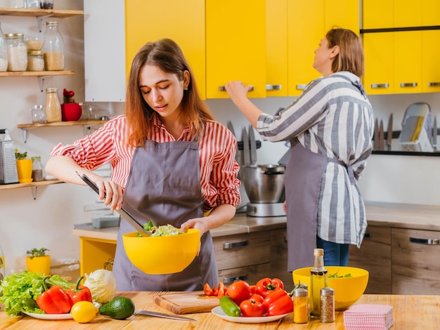 Family leisure Daughter helping her mother prepare vegetable salad in modern kitchen