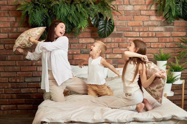 Family leisure. Mom son and daughter fight on pillows on the bed in the bedroom.