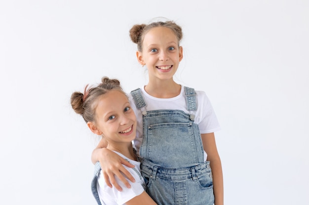 Family and love concept - two smiling twin sisters hugging over white background