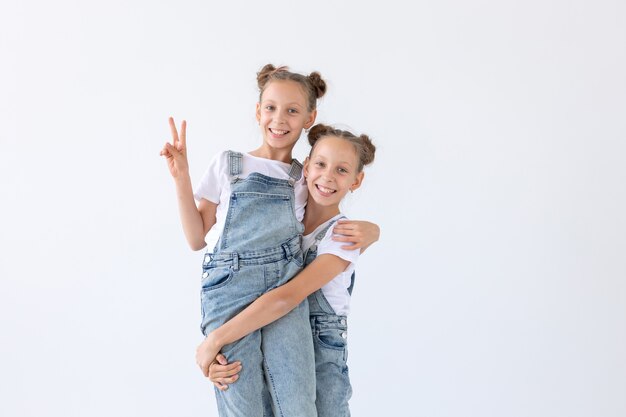 Famiglia e concetto di amore - due sorelle gemelle sorridenti che abbracciano sopra il muro bianco.