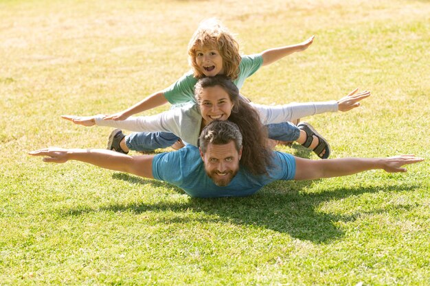 Famiglia sdraiata sull'erba nel parco concetto di volo il ragazzino è seduto pickaback mentre imita il volo