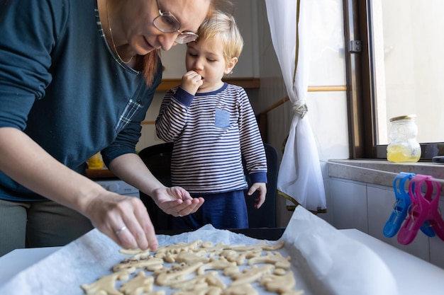 クッキーを作る家族と幼い息子を持つ女性が生地に砂糖をまぶす