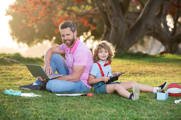 Padre e figlio online di affari dell'uomo di famiglia che lavorano sul telecomando del computer portatile nel parco