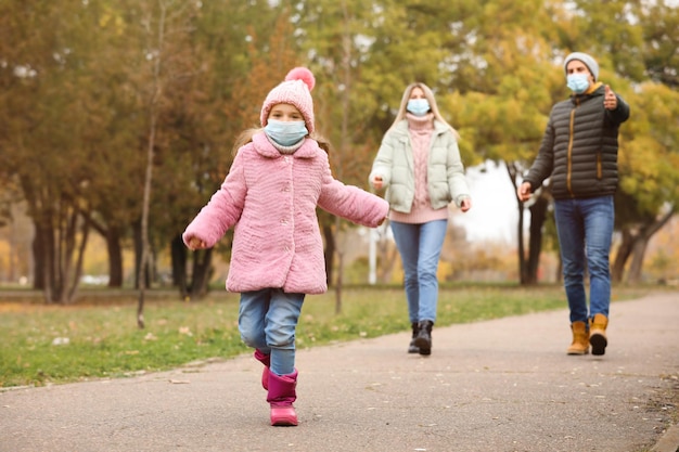 Family in medical masks walking outdoors on autumn day Protective measures during coronavirus quarantine